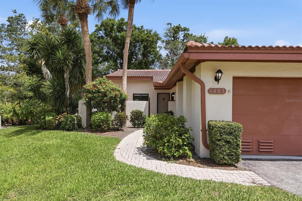 A paved walkway leads to the entrance of a house with a tan garage door — 6403 PELICAN DRIVE, BRADENTON, FL