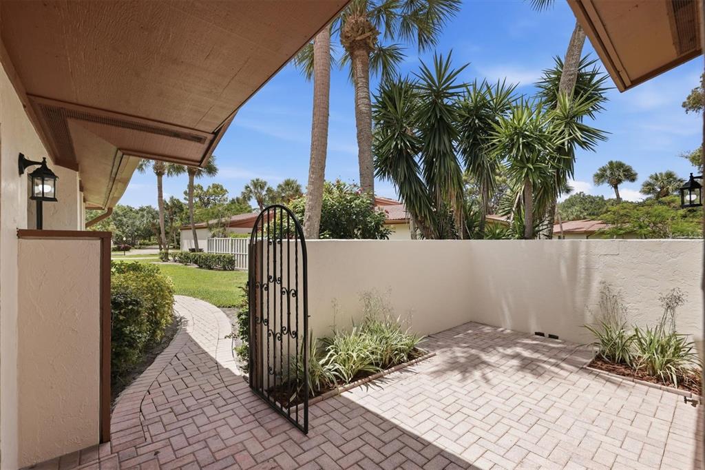 A paved patio area features a wrought iron gate, stucco walls, and surrounding palm trees — 6403 PELICAN DRIVE, BRADENTON, FL