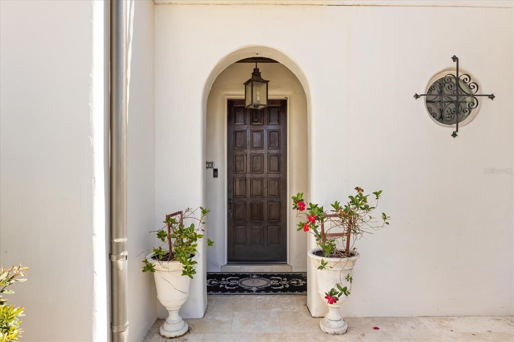 An arched wooden front door is flanked by two large potted plants on a patio — 12411 MONTALCINO CIRCLE, WINDERMERE, FL