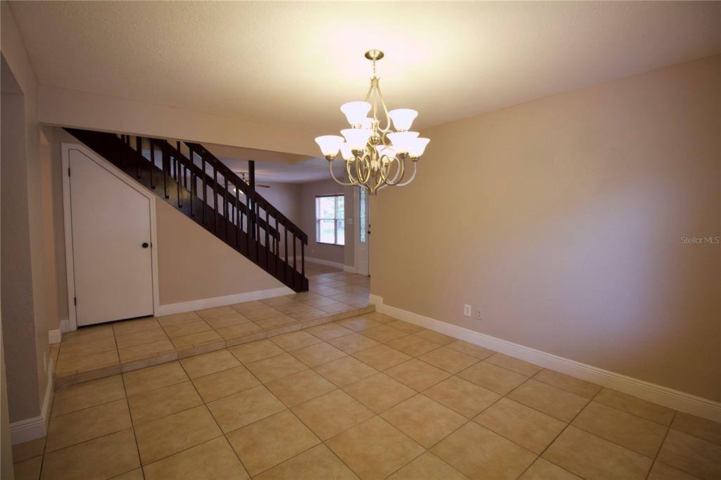 A dining room features tan tile flooring, a chandelier, and a staircase with dark railings — 1817 LAURENCE COURT, CLEARWATER, FL