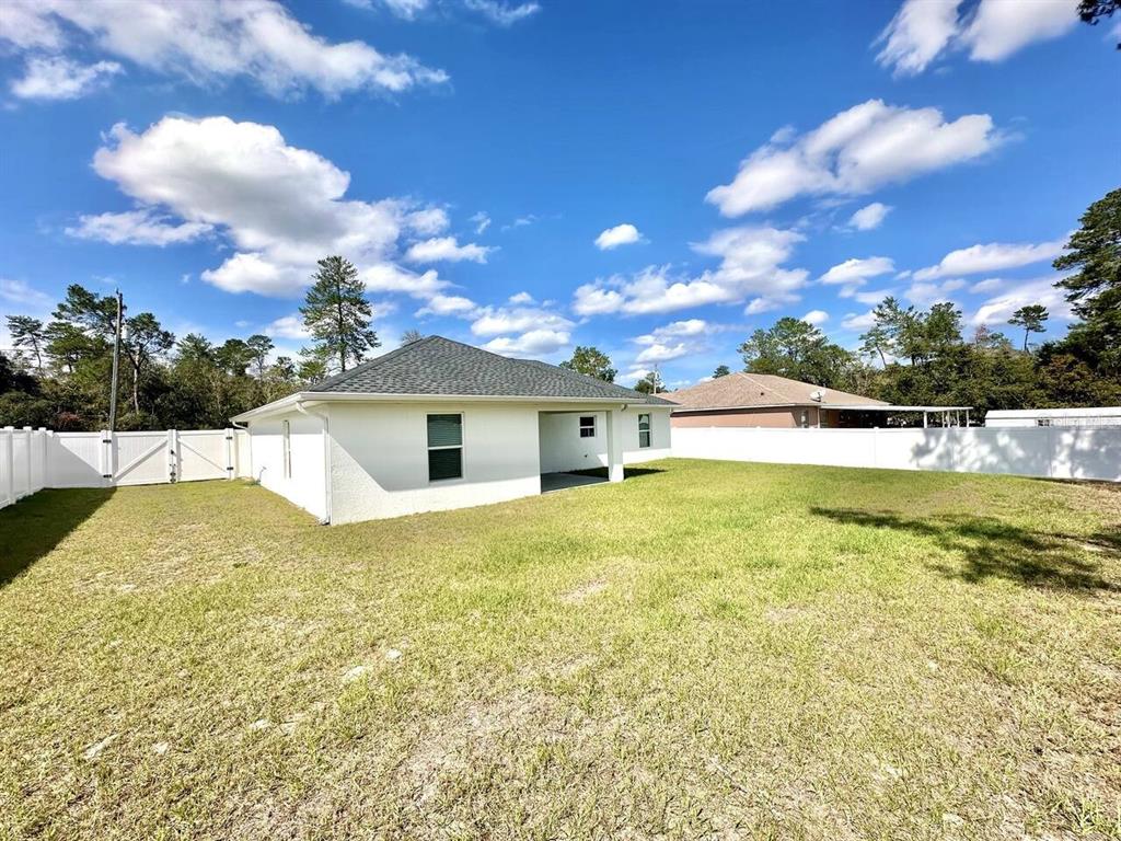 The rear exterior of a white house features a covered patio and a fenced yard — 2409 SW 156TH LOOP, OCALA, FL