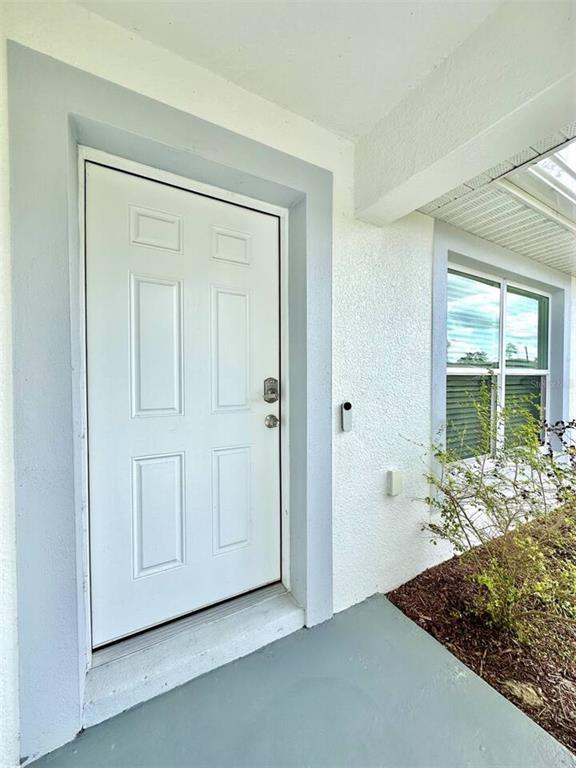 A white six-panel front door with a smart doorbell is set in a stucco exterior — 2409 SW 156TH LOOP, OCALA, FL