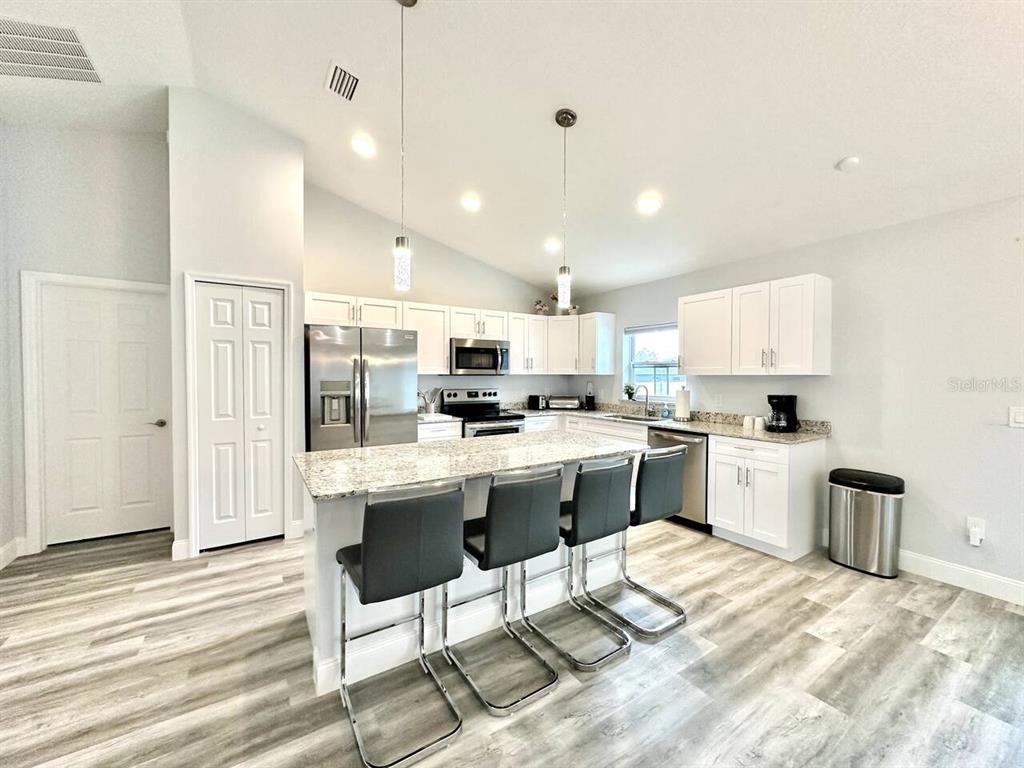 A modern kitchen features white cabinets, granite countertops, a center island, and gray wood-look flooring — 2409 SW 156TH LOOP, OCALA, FL