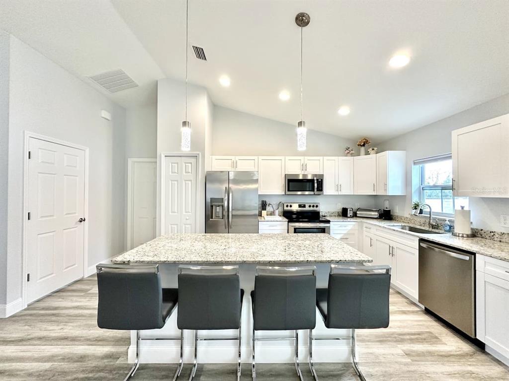 A kitchen with white cabinets, granite countertops, a center island, and four gray bar stools — 2409 SW 156TH LOOP, OCALA, FL