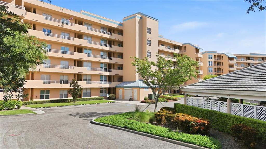 An exterior view of a multi-story, peach-colored apartment building with balconies and a parking area — 4570 PINEBROOK CIRCLE UNIT 503, BRADENTON, FL