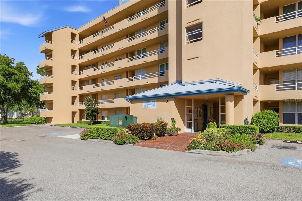 A multi-story tan apartment building features a covered entrance and a paved parking lot — 4570 PINEBROOK CIRCLE UNIT 503, BRADENTON, FL