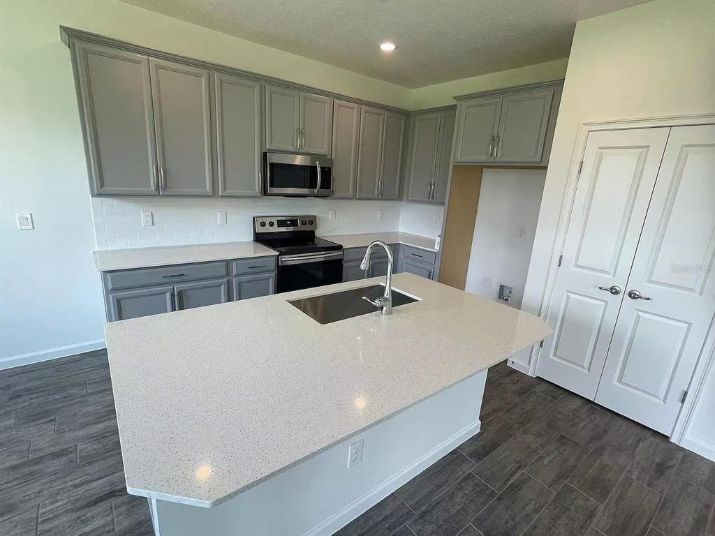 A kitchen features gray cabinets, white countertops, a center island with a sink, and tile flooring — 1365 YORKDALE ROAD, DAVENPORT, FL