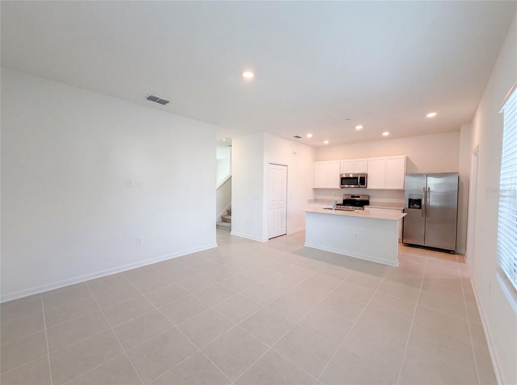 An open-concept kitchen with white cabinetry and stainless steel appliances overlooks a tiled living area — 2224 RED SUN STREET, APOPKA, FL