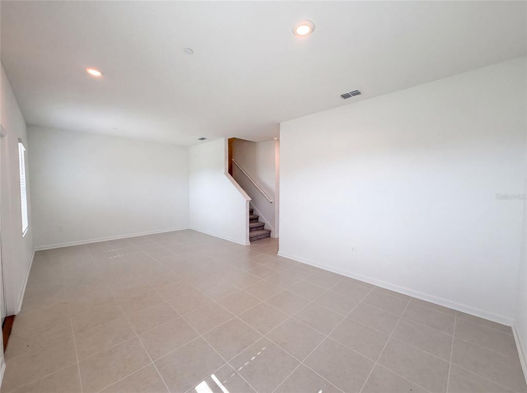 An empty room with light-colored tile flooring, white walls, recessed lighting, and a carpeted staircase — 2224 RED SUN STREET, APOPKA, FL