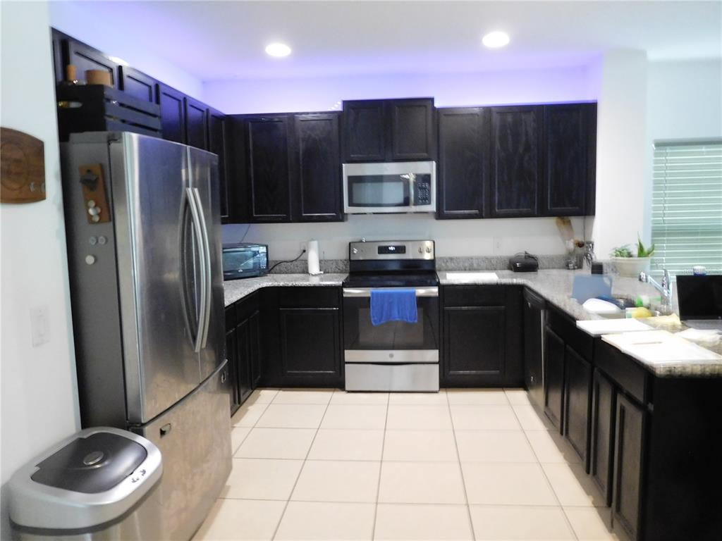 A kitchen features dark wood cabinets, stainless steel appliances, granite countertops, and light tile flooring — 4767 MARCOS CIRCLE, KISSIMMEE, FL