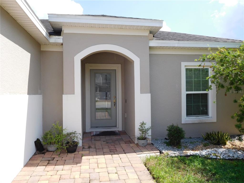 The exterior of a house features a paved walkway leading to a gray front door — 4767 MARCOS CIRCLE, KISSIMMEE, FL