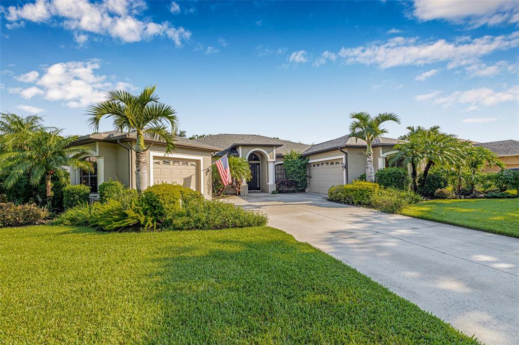A single-story house with a concrete driveway, palm trees, and an American flag — 15420 27TH COURT E, PARRISH, FL