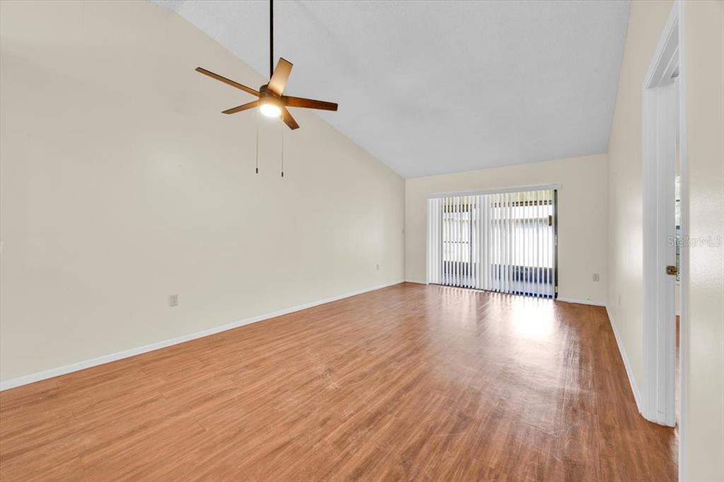 An empty room features light-colored walls, wood-look flooring, a ceiling fan, and sliding glass doors — 2907 PRINCE OAK COURT, ST CLOUD, FL