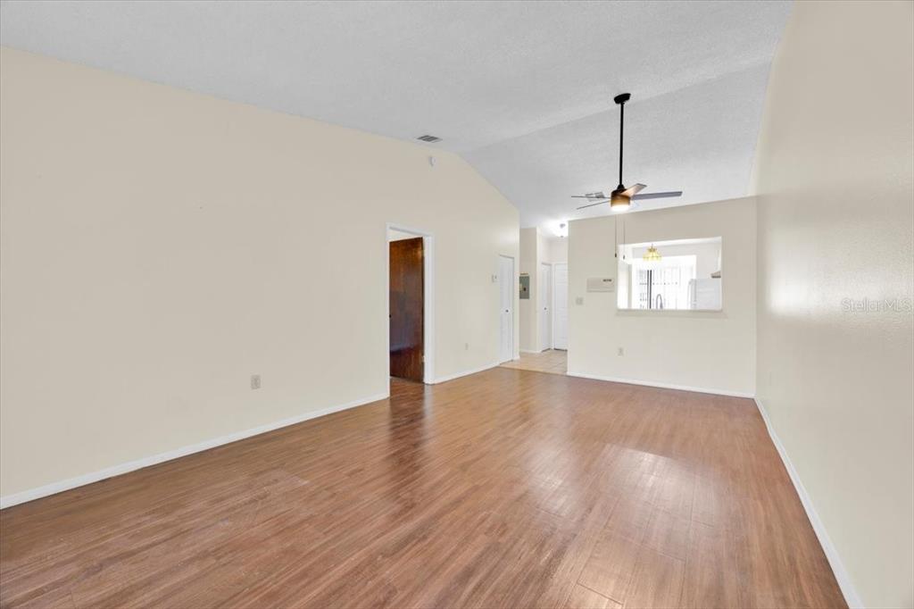 An empty living room features wood-look flooring, a vaulted ceiling, and a ceiling fan — 2907 PRINCE OAK COURT, ST CLOUD, FL