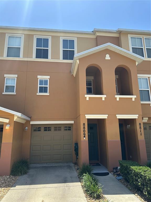 A three-story townhouse exterior features a tan stucco facade, a single-car garage, and arched entryways — 8809 WHITE SAGE LOOP, LAKEWOOD RANCH, FL
