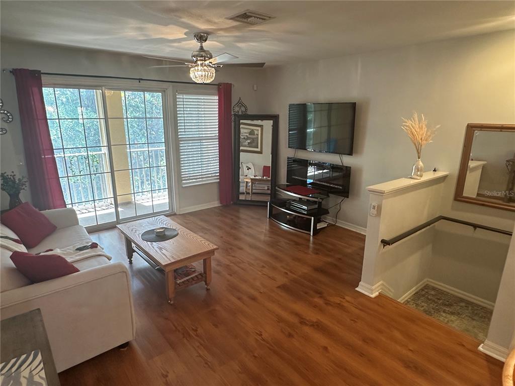 A living room features wood-look flooring, a sliding glass door, and a staircase with railing — 8809 WHITE SAGE LOOP, LAKEWOOD RANCH, FL