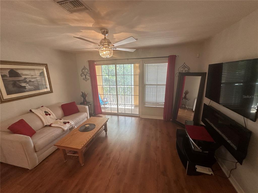 A living room features wood-look flooring, a ceiling fan, a sofa, and a television — 8809 WHITE SAGE LOOP, LAKEWOOD RANCH, FL