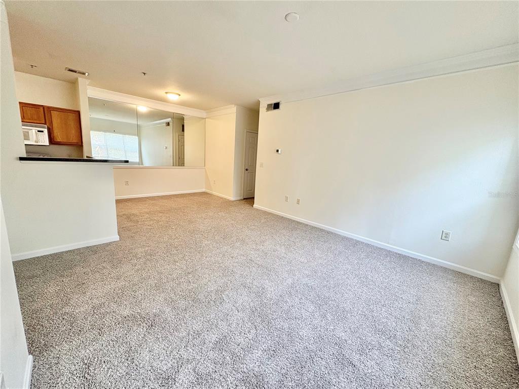 A carpeted living room features a mirrored wall and an open view into the kitchen — 4802 51ST STREET W UNIT 1016, BRADENTON, FL