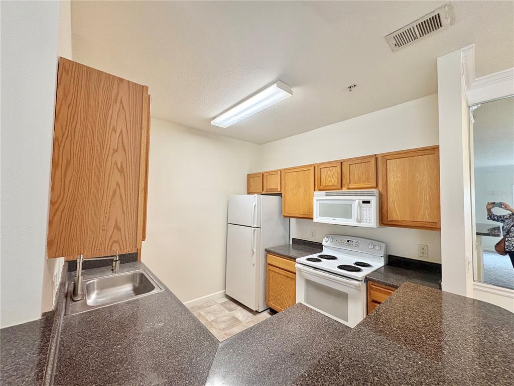 A kitchen features oak cabinets, dark countertops, white appliances, and a stainless steel sink — 4802 51ST STREET W UNIT 1016, BRADENTON, FL