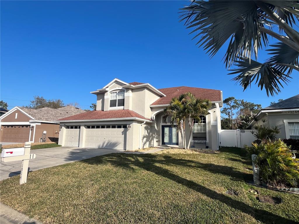 A two-story house with a beige stucco exterior, a three-car garage, and a palm tree — 1914 OSWEGO DRIVE, HOLIDAY, FL