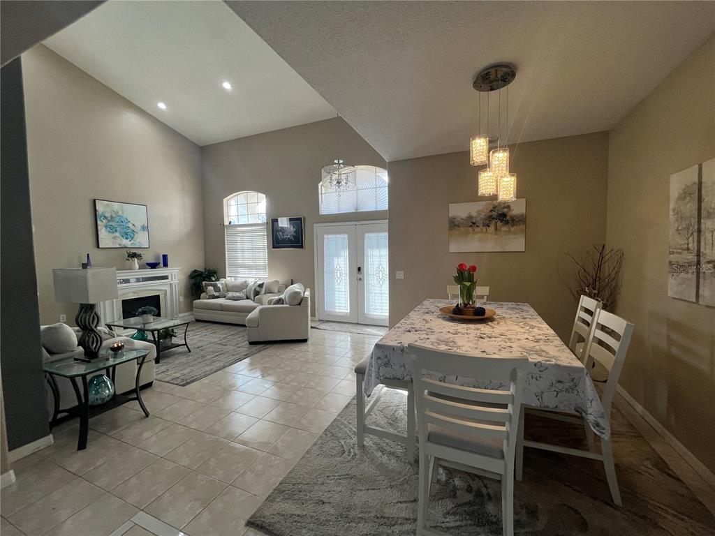 An open-concept living and dining area features vaulted ceilings, tile flooring, and a fireplace — 1914 OSWEGO DRIVE, HOLIDAY, FL