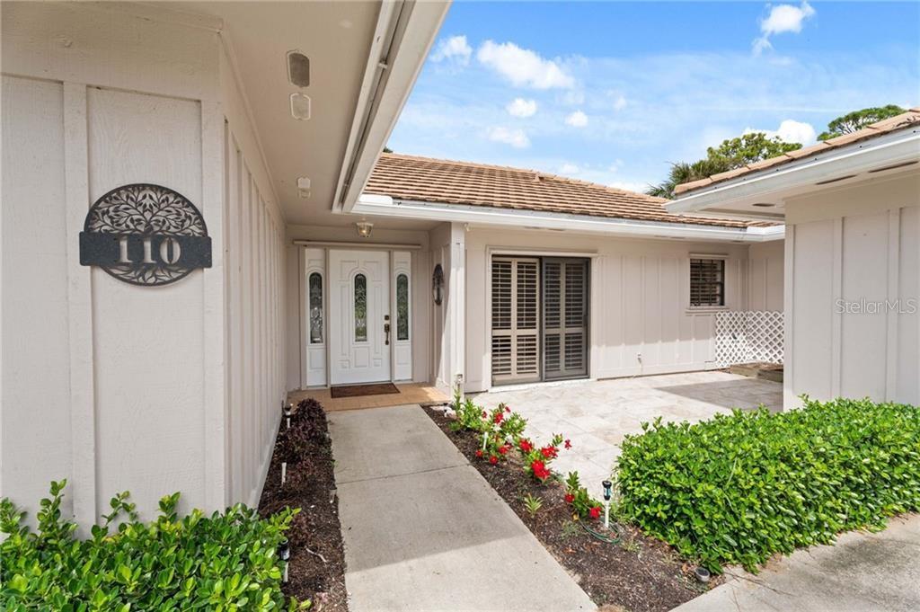 A concrete walkway leads to the front entrance of a house with light-colored siding — 110 PRESTWICK CIRCLE, VERO BEACH, FL