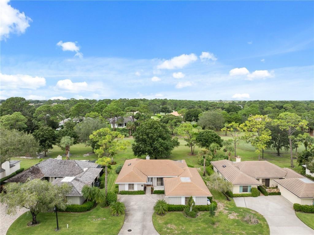An aerial view shows three suburban houses with tiled roofs surrounded by trees and grass — 110 PRESTWICK CIRCLE, VERO BEACH, FL