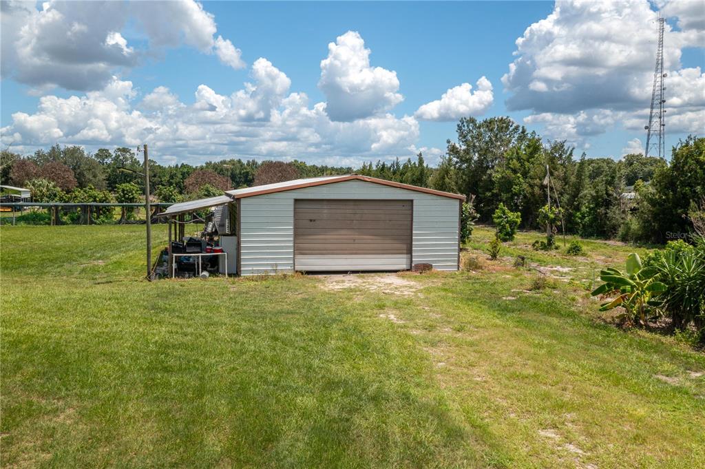 A detached metal garage with a roll-up door sits on a grassy lot under clouds — 270 KEEN ROAD, FROSTPROOF, FL