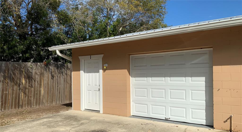 An exterior view of a tan concrete block garage with a white door and garage door — 2417 GUAVA DRIVE UNIT 1, EDGEWATER, FL