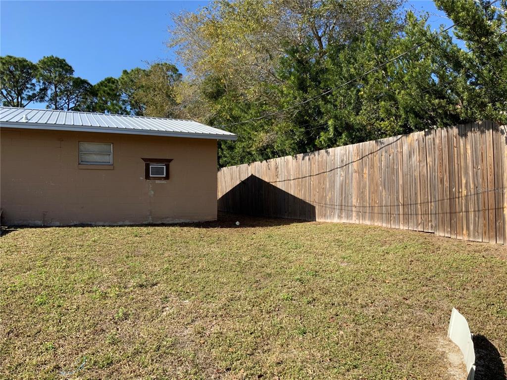 A tan concrete block building stands next to a wooden privacy fence in a yard — 2417 GUAVA DRIVE UNIT 1, EDGEWATER, FL