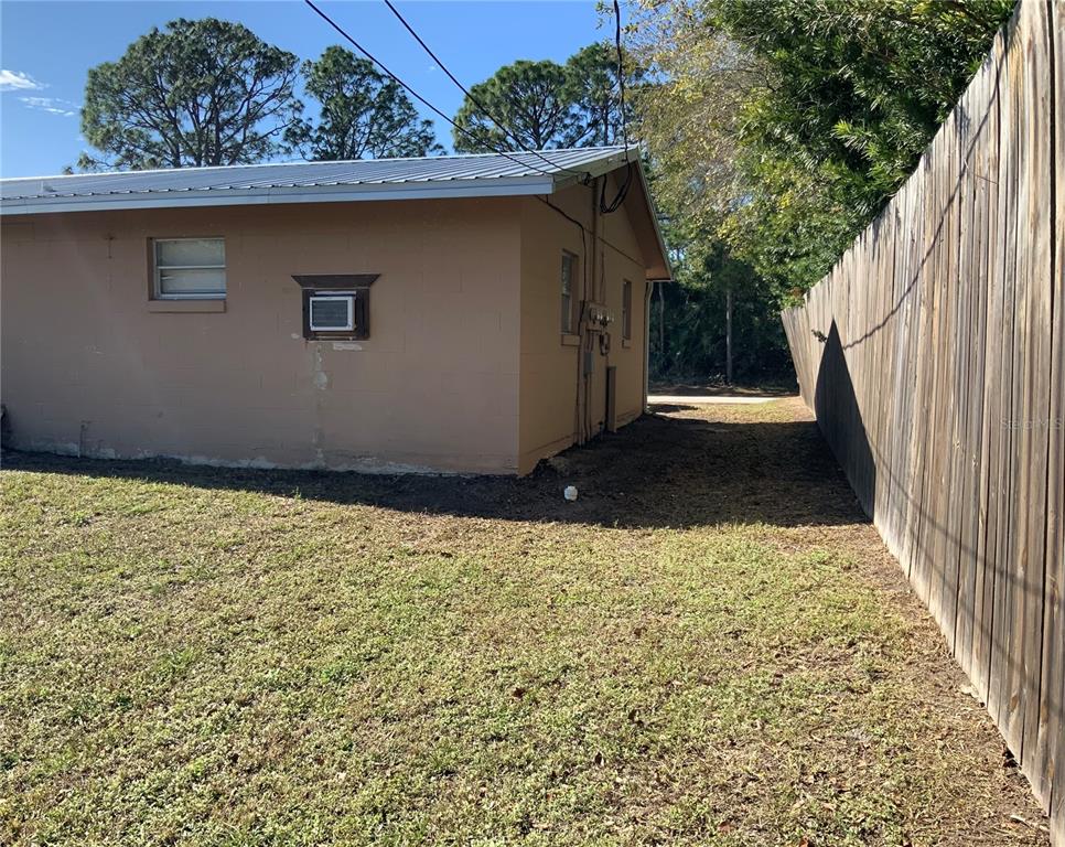 The exterior side of a tan concrete block house with a metal roof and fence — 2417 GUAVA DRIVE UNIT 1, EDGEWATER, FL