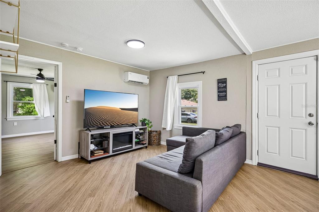 A living room features light wood flooring, a gray sectional sofa, and a wall-mounted television — 1903 N BARNES STREET, PLANT CITY, FL