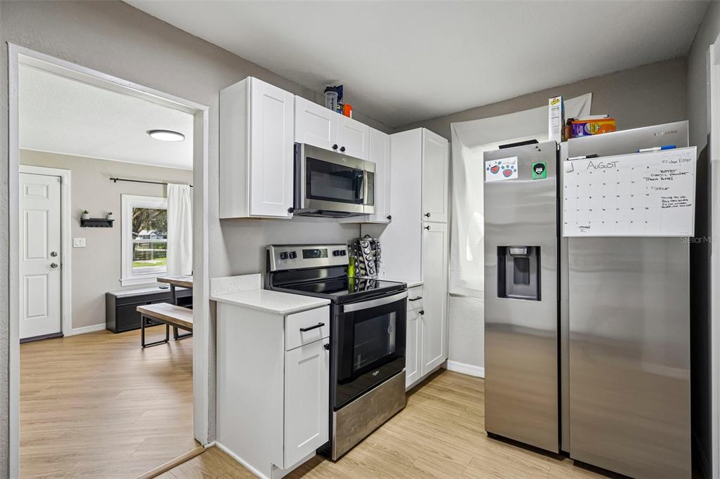 A kitchen features white cabinets, stainless steel appliances, and light wood-look flooring — 1903 N BARNES STREET, PLANT CITY, FL