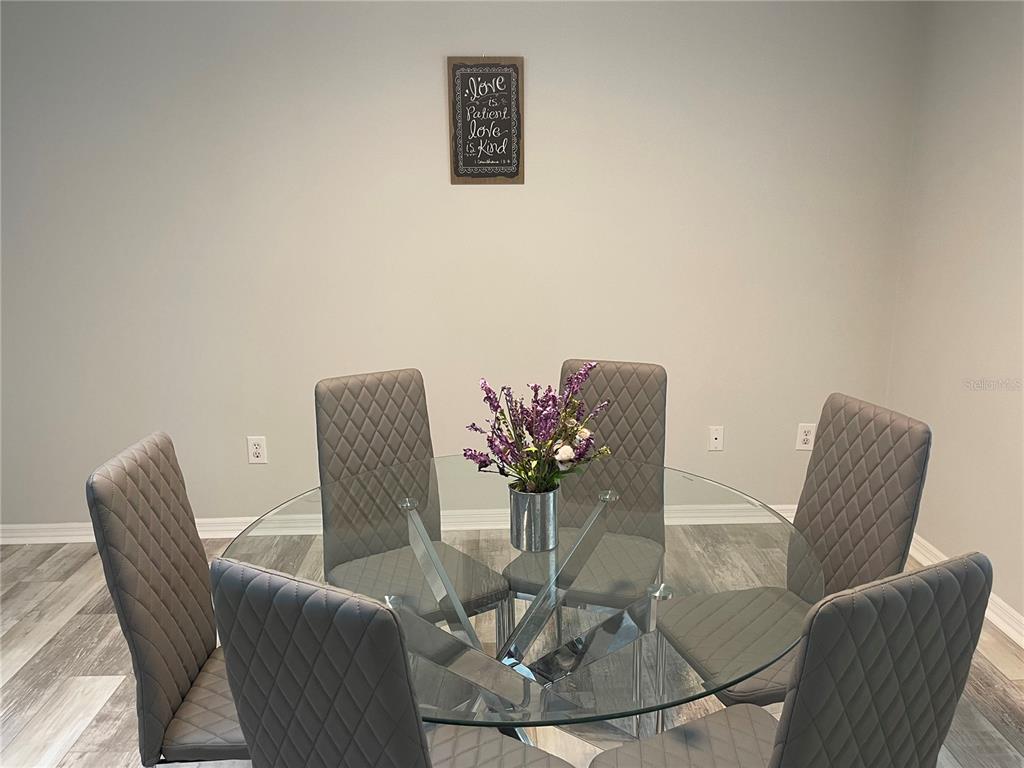 A dining room features a round glass table with six gray quilted chairs on wood-look flooring — 21 POST VIEW DRIVE, PALM COAST, FL