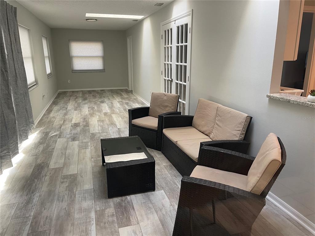 A sunroom features light wood-look flooring, a glass-topped coffee table, and wicker patio furniture — 21 POST VIEW DRIVE, PALM COAST, FL