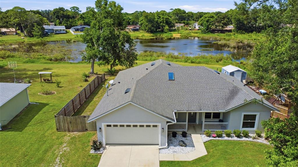 An aerial view of a single-story house with a garage, gray roof, and backyard pond — 120 FLORIDANA ROAD, DEBARY, FL