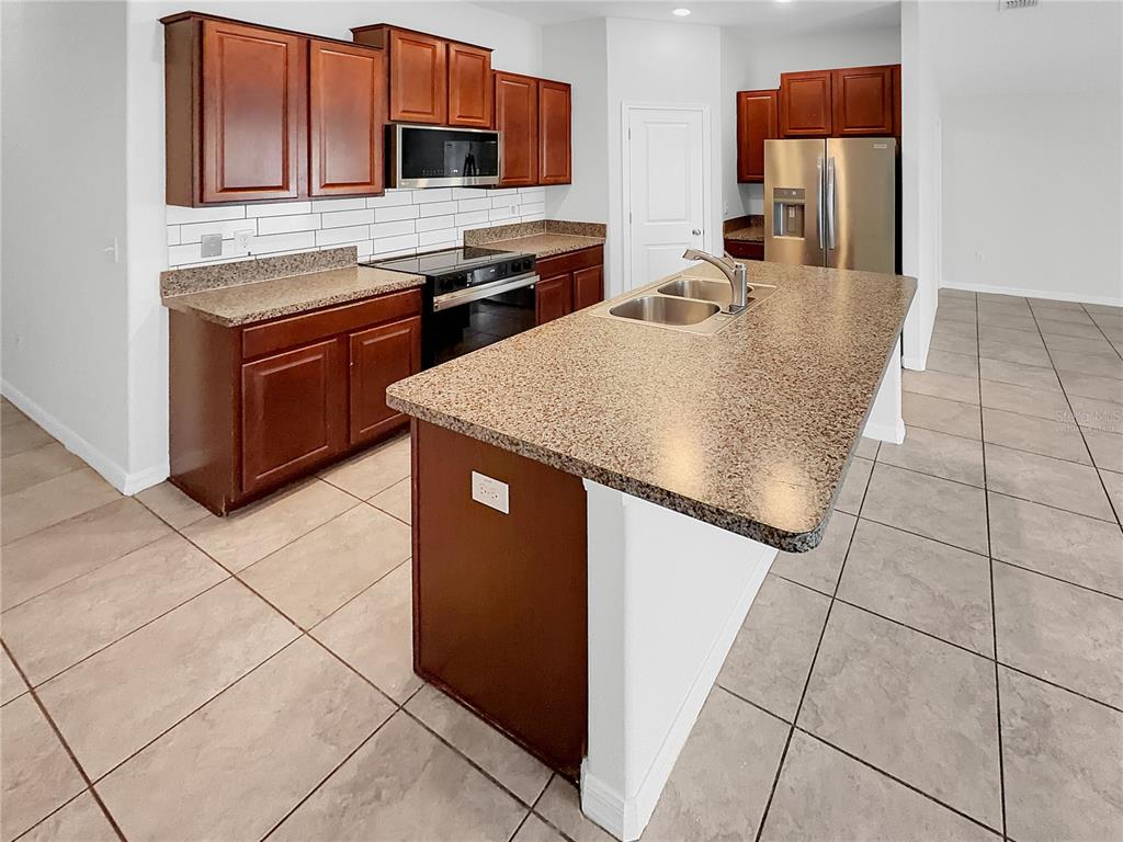 A kitchen features dark wood cabinets, granite countertops, a central island, and tile flooring — 10113 ROSEMARY LEAF LANE, RIVERVIEW, FL