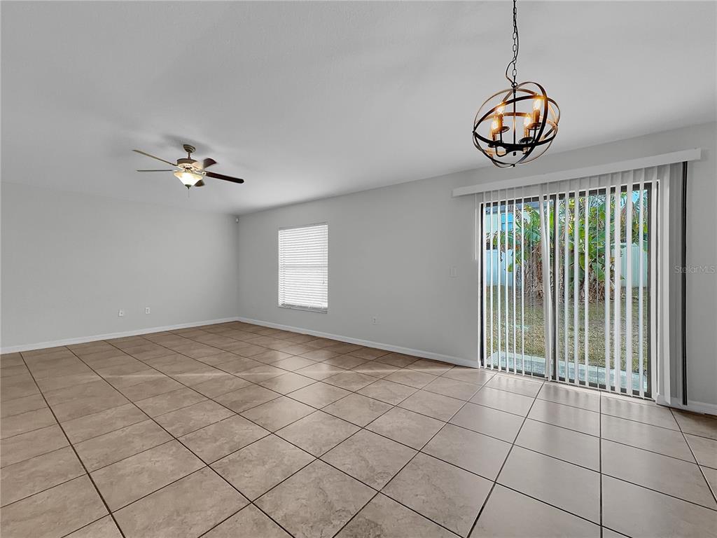 An empty room with tile flooring, a ceiling fan, a chandelier, and sliding glass doors — 10113 ROSEMARY LEAF LANE, RIVERVIEW, FL
