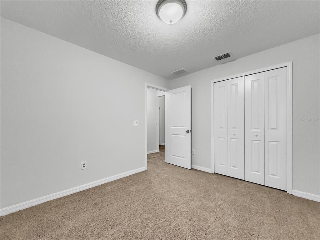 A bedroom with light gray walls, beige carpet, a white closet, and an open doorway — 10113 ROSEMARY LEAF LANE, RIVERVIEW, FL