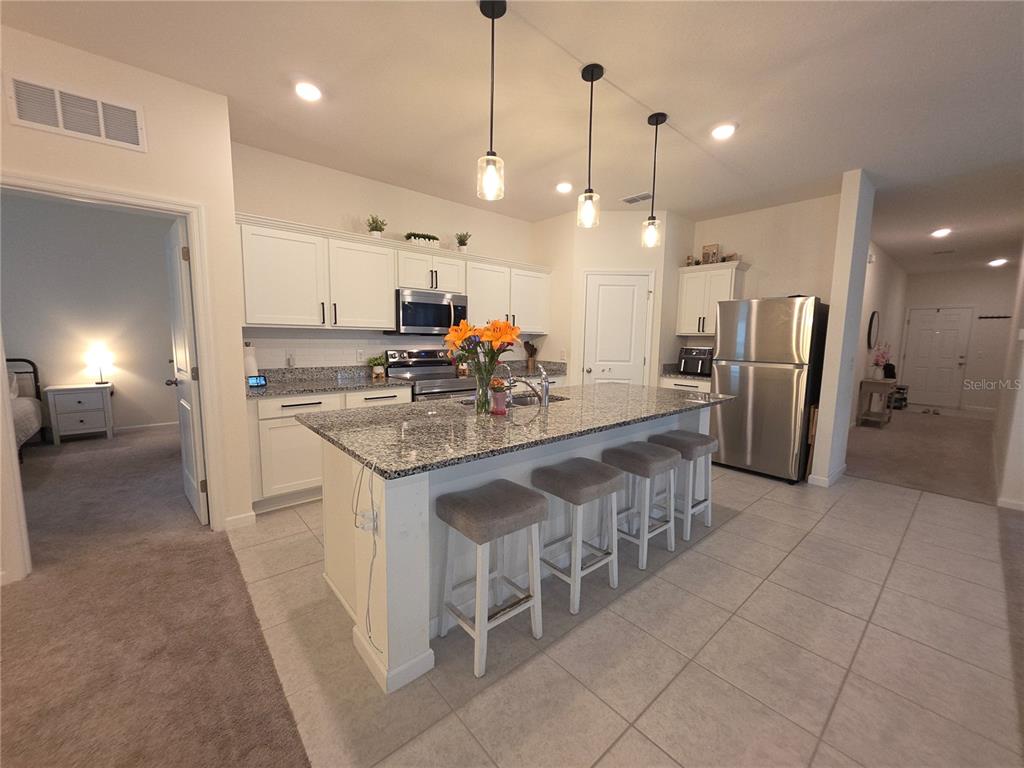 A kitchen features white cabinets, granite countertops, a central island with bar seating, and stainless appliances — 1569 EFFRA WAY, SANFORD, FL