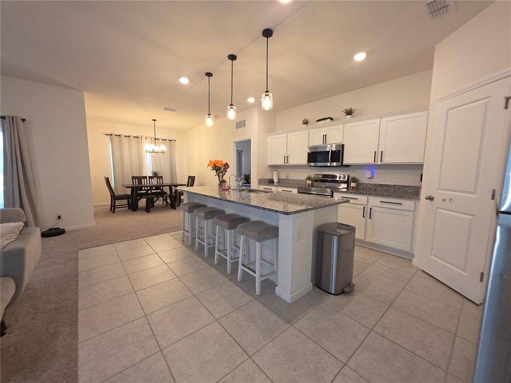 A kitchen with a granite island, white cabinets, and stainless steel appliances opens to a dining area — 1569 EFFRA WAY, SANFORD, FL