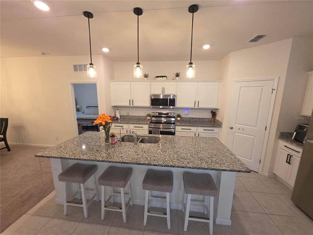 A kitchen features a large granite-topped island with four stools and white cabinetry — 1569 EFFRA WAY, SANFORD, FL