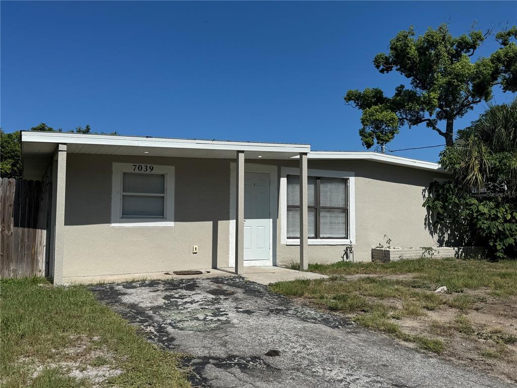 A single-story house with a beige exterior, a covered entryway, and a weathered asphalt driveway — 7039 E LENOX DRIVE E, NEW PORT RICHEY, FL