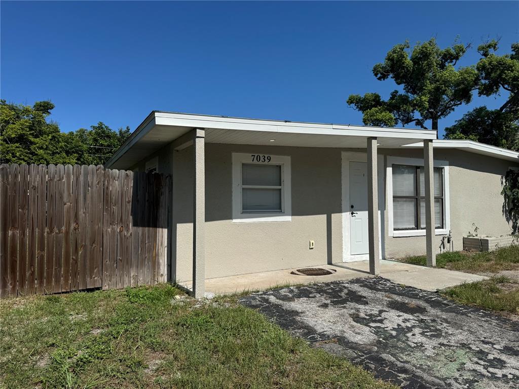 A single-story house with a beige exterior, a covered porch, and a wooden privacy fence — 7039 E LENOX DRIVE E, NEW PORT RICHEY, FL