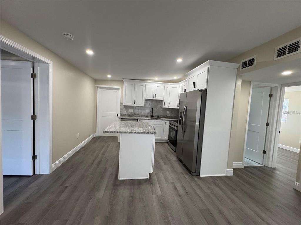 A kitchen features white cabinets, granite countertops, stainless steel appliances, and gray wood-look flooring — 7039 E LENOX DRIVE E, NEW PORT RICHEY, FL