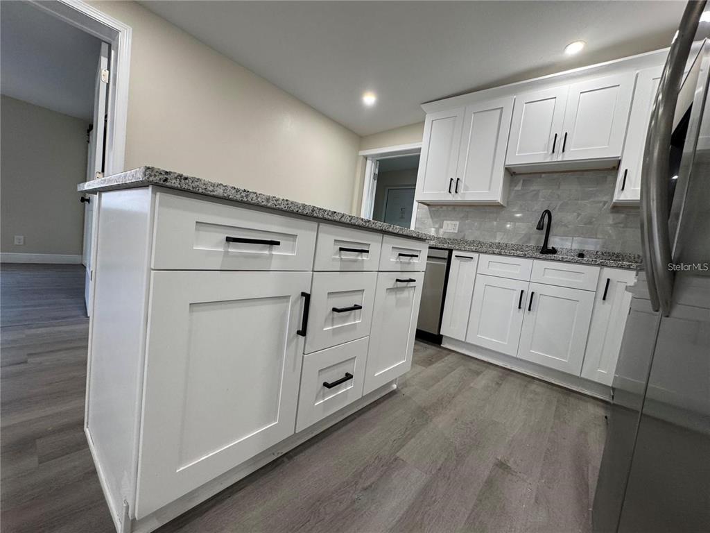 A kitchen features white cabinets, granite countertops, a center island, and wood-look flooring — 7039 E LENOX DRIVE E, NEW PORT RICHEY, FL