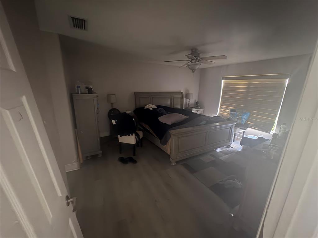 A bedroom features light wood-look flooring, a gray bed frame, and a ceiling fan — 128 SPINNAKER CIRCLE, SOUTH DAYTONA, FL