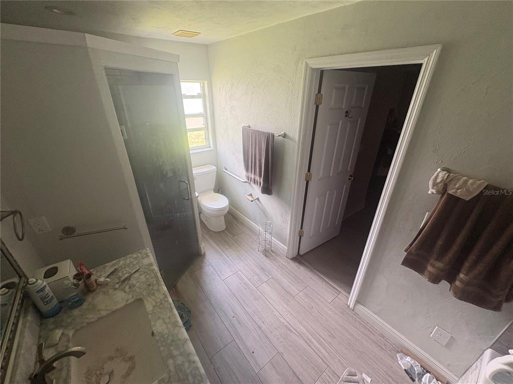 A bathroom features a glass shower, a toilet, a vanity, and light wood-look tile flooring — 128 SPINNAKER CIRCLE, SOUTH DAYTONA, FL