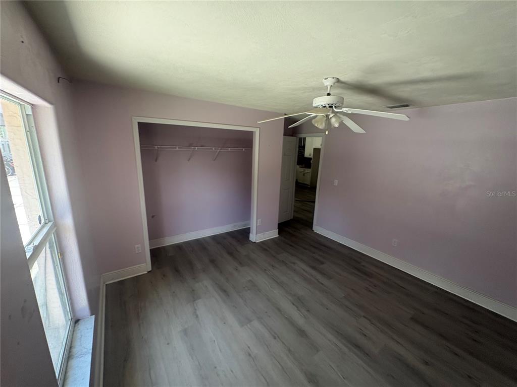 A bedroom with light purple walls, wood-look flooring, a ceiling fan, and an open closet — 128 SPINNAKER CIRCLE, SOUTH DAYTONA, FL
