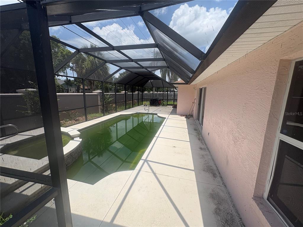 A screened-in patio features a pool and spa with green water next to a house — 128 SPINNAKER CIRCLE, SOUTH DAYTONA, FL
